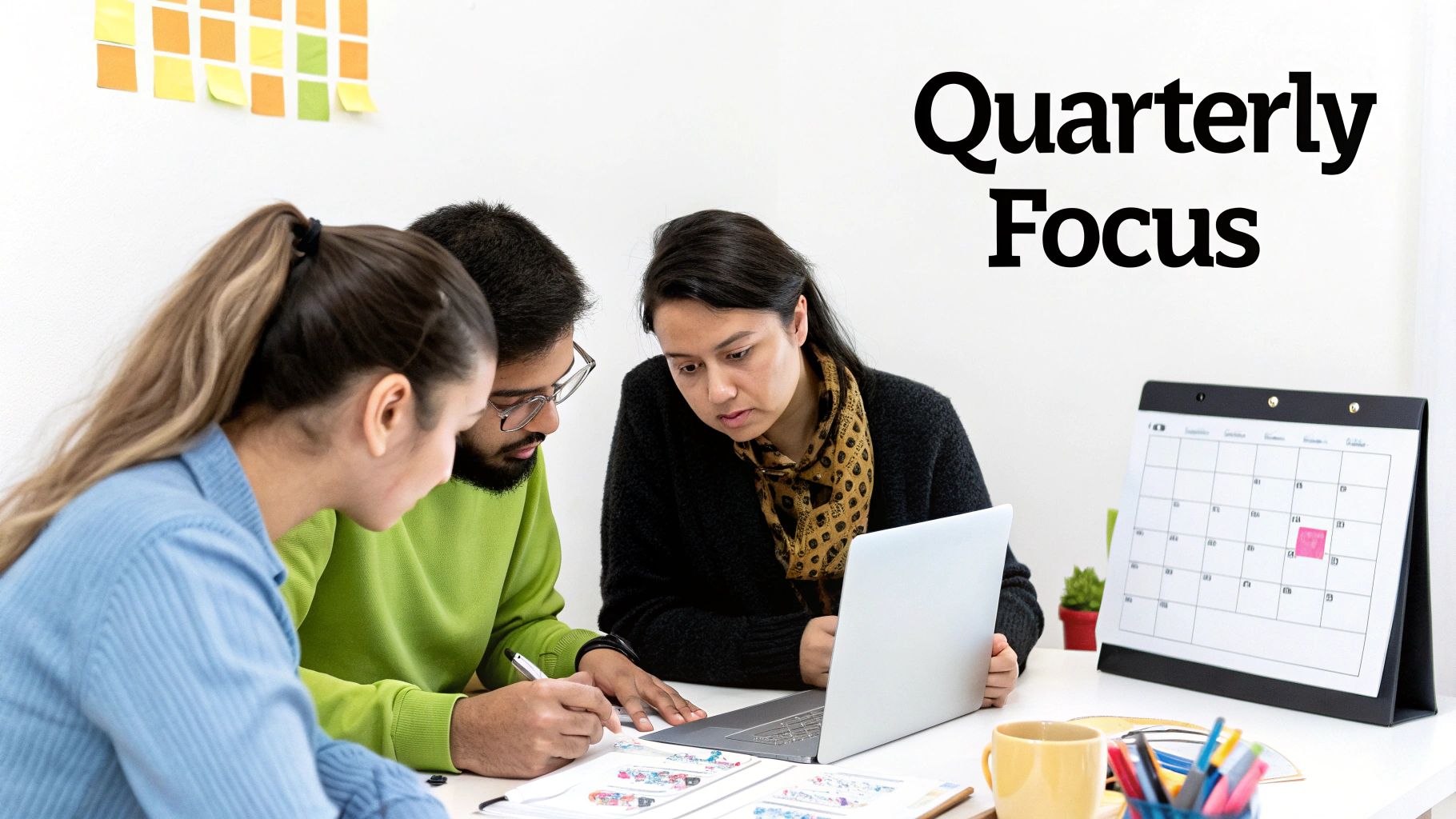 Three people collaborate at a desk with a laptop, planning their quarterly focus with notes and a calendar.
