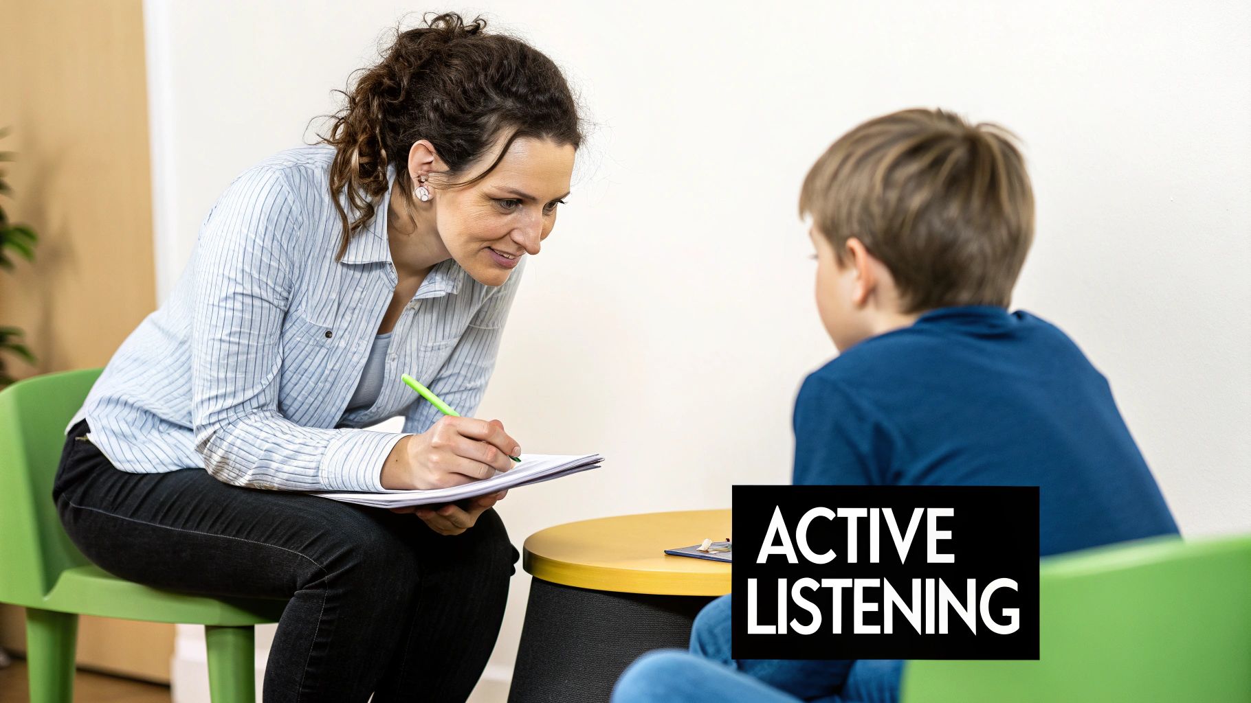 A female tutor actively listens and takes notes while a young boy sits, demonstrating effective communication.