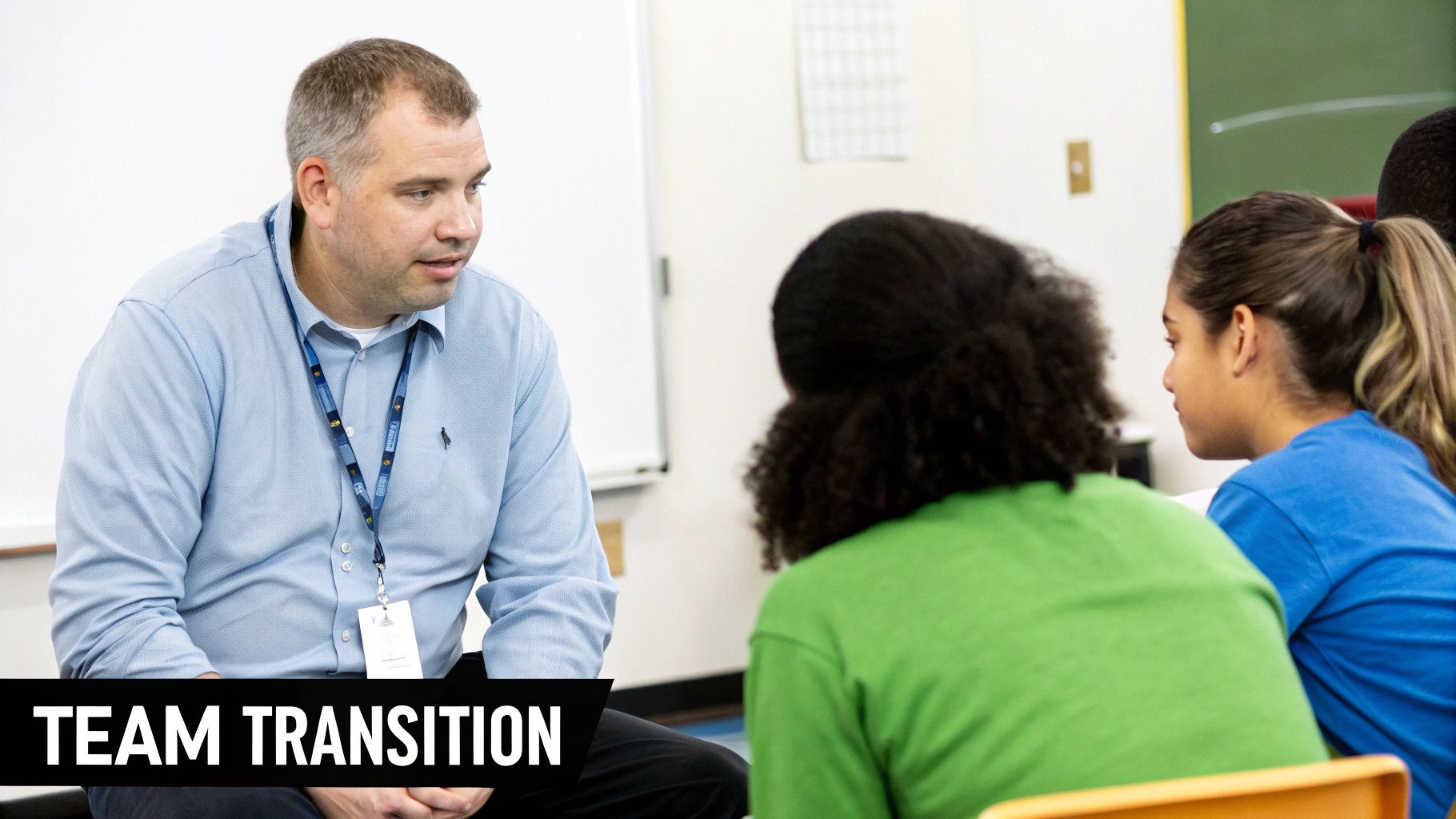 A male mentor in a blue shirt speaking with two female students in a classroom.