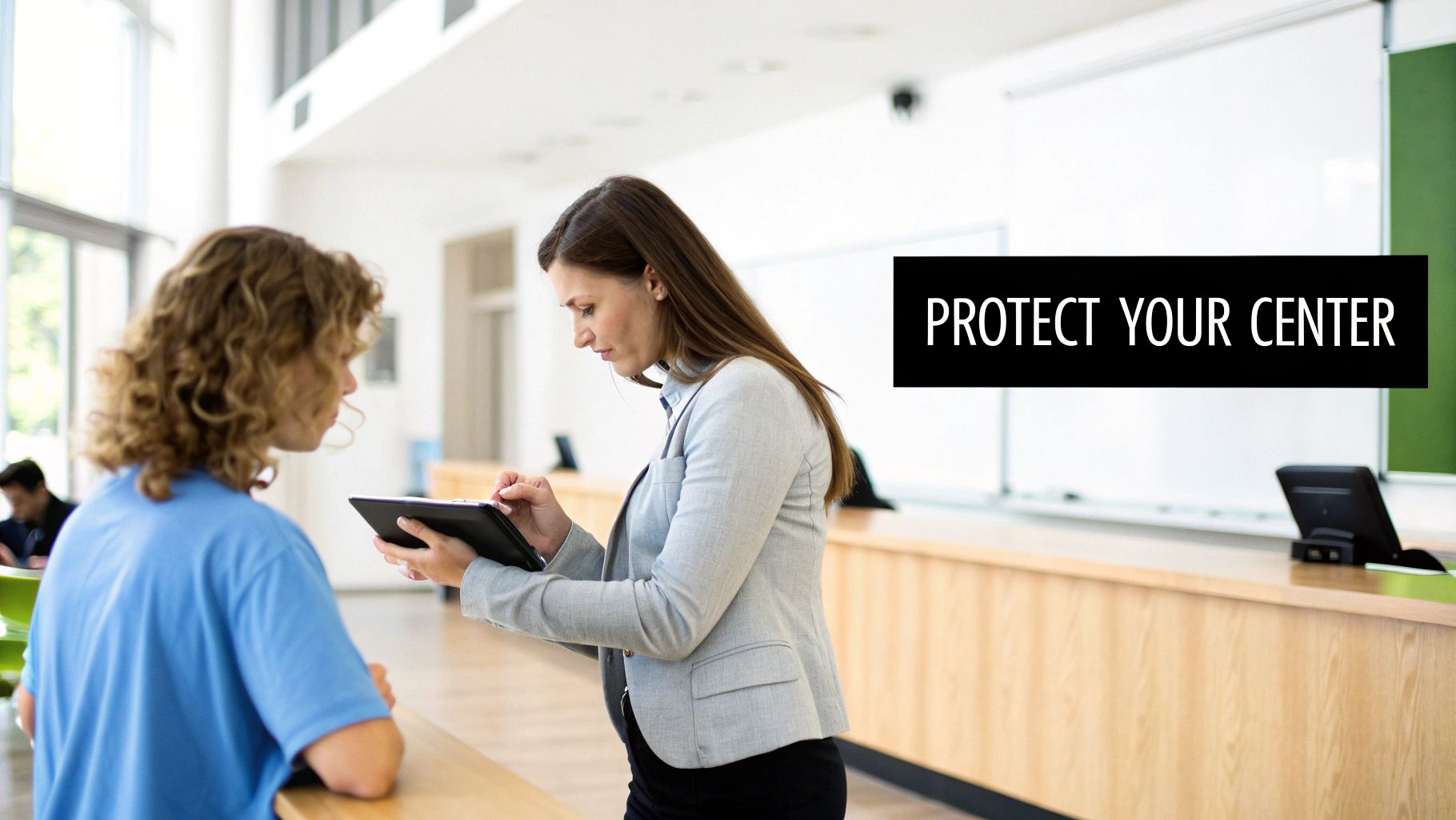 A professional woman uses a tablet and stylus while consulting with a student in a bright classroom.